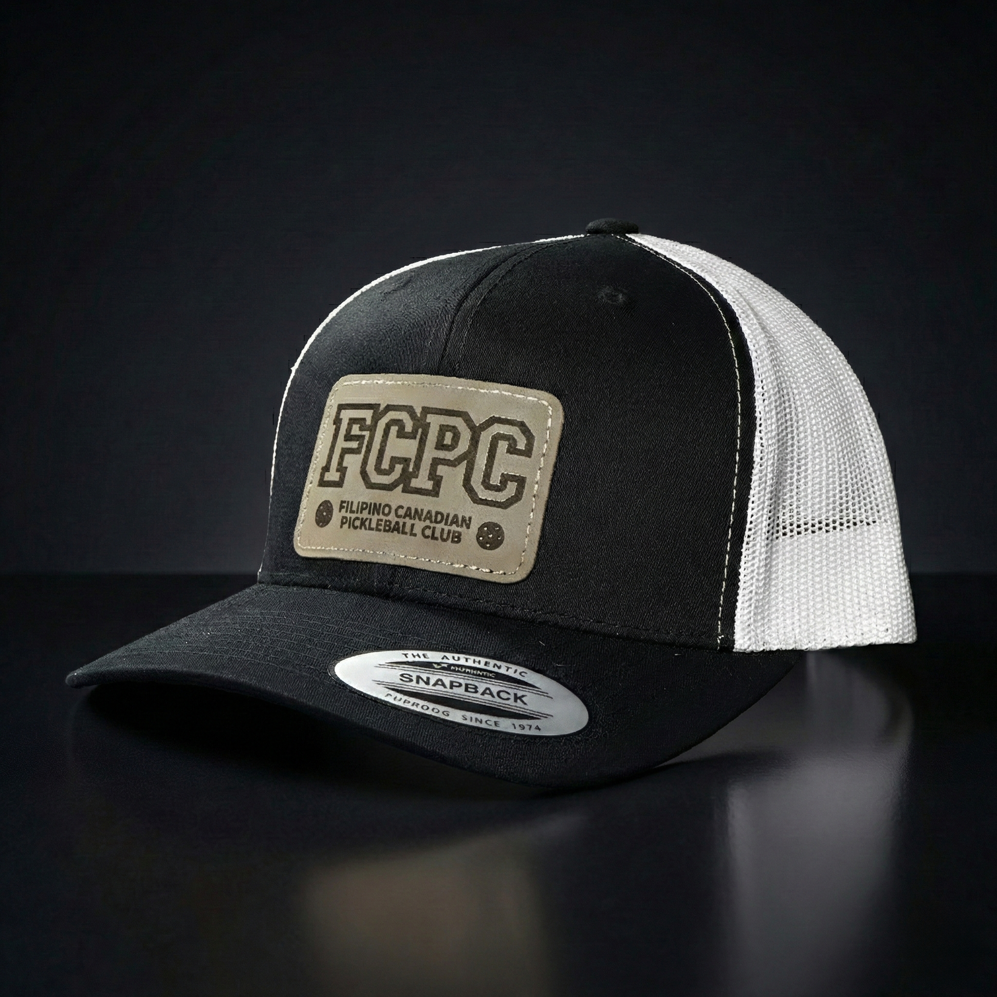 Black and white trucker cap with FCPC logo on a dark background